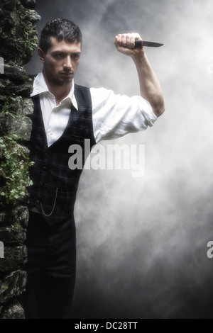 a man hiding behind a wall with a knife Stock Photo