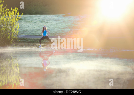 Teenage girl stretching by misty lake in sunlight Stock Photo