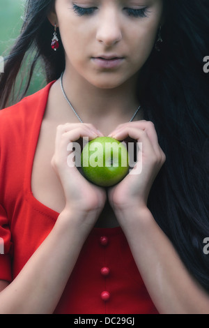 a woman in a red dress, holding a green apple