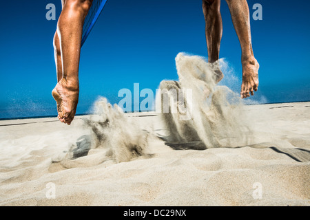 Two beach volleyball players jumping mid air in sand Stock Photo