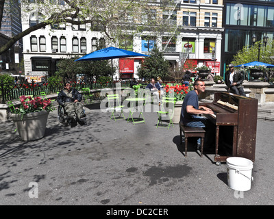 happy young man plays beat up piano for sparse audience including man in wheelchair on beautiful sunny spring day Union Square Stock Photo