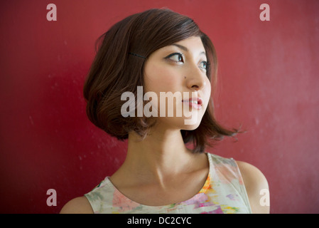 Woman against red wall looking into distance Stock Photo