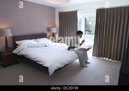 Man sitting on bed looking at digital tablet