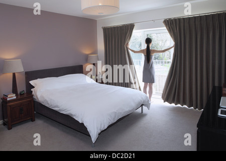 Woman drawing open curtains of bedroom Stock Photo