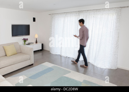 Man with mobile phone walking past curtains Stock Photo