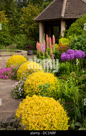 Summer flower boarder with purple Allium, delphiniums and foxgloves with stone summerhouse in English garden, England Stock Photo