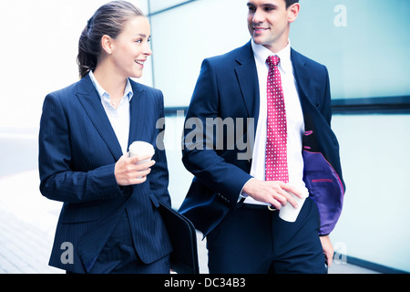 Smiling businessman and businesswoman walking with coffee Stock Photo