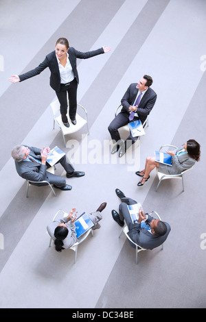 High angle view of businesswoman standing on chair in circle with co-workers Stock Photo