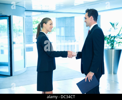 Smiling businessman and businesswoman handshaking in lobby Stock Photo