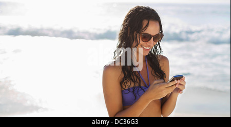 Smiling woman text messaging with cell phone on beach Stock Photo