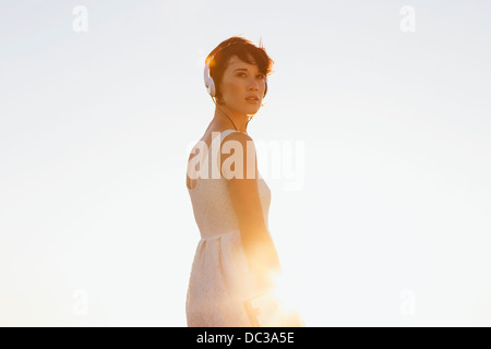 Pensive woman in dress wearing headphones and looking back Stock Photo
