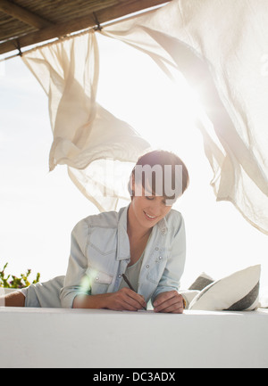 Smiling woman writing on sunny patio Stock Photo