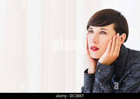 Pensive woman with head in hands looking out window Stock Photo