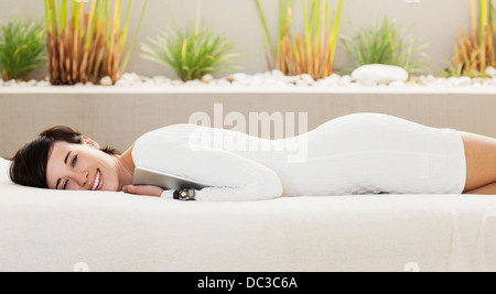 Portrait of smiling woman holding digital tablet and laying on patio sofa