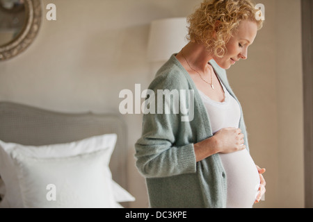 Smiling pregnant woman touching stomach in bedroom Stock Photo