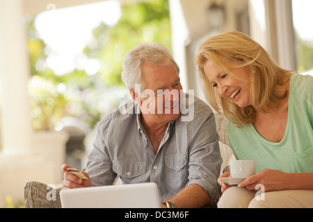 Smiling couple drinking coffee and shopping online on patio Stock Photo