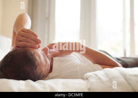 Man laying in bed with head in hands Stock Photo