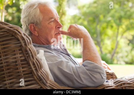 Pensive senior man sitting in wicker armchair on porch Stock Photo