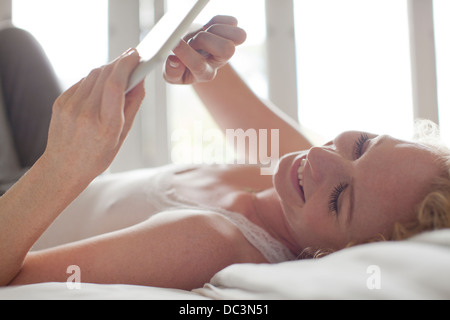 Smiling woman laying in bed and using digital tablet Stock Photo