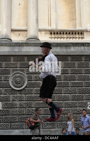 Man walking on tightrope whilst playing violin, Busker / Street Entertainer in Bath city centre England Stock Photo