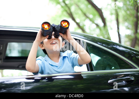 Cheerful boy leaning out of car window and looking with binoculars Stock Photo