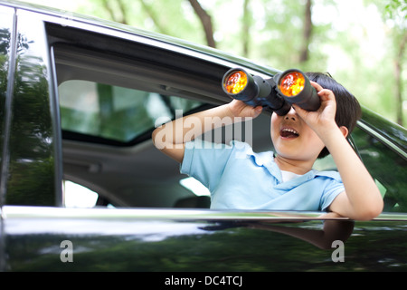 Cheerful boy leaning out of car window and looking with binoculars Stock Photo