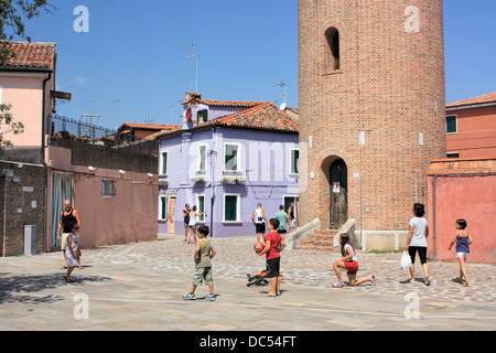 Kids playing on the streets of Burano Island, Isola di Burano Island, Venice, Italy. Water tower in the background. Stock Photo