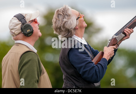 Lady shooting a shotgun at a simulated game clay shooting day, helped by a loader Stock Photo