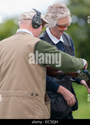 Lady shooting a shotgun at a simulated game clay shooting day, helped by a loader loading her gun Stock Photo