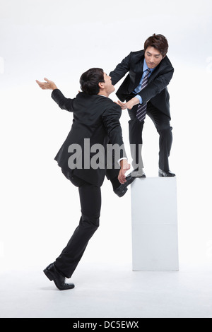 a businessman trying to push away a man from climbing up Stock Photo