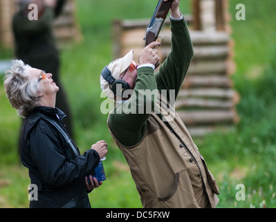 Man shooting a shotgun at a simulated game and grouse clay shooting day with a lady loader Stock Photo