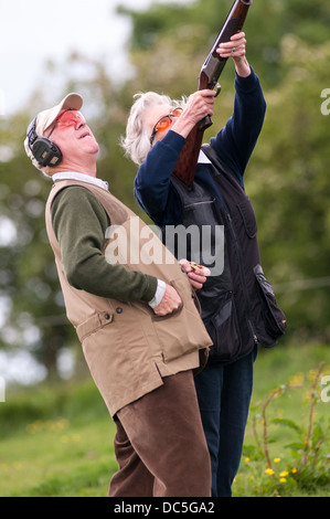 Lady shooting a shotgun at a simulated game clay shooting day, helped by a loader Stock Photo