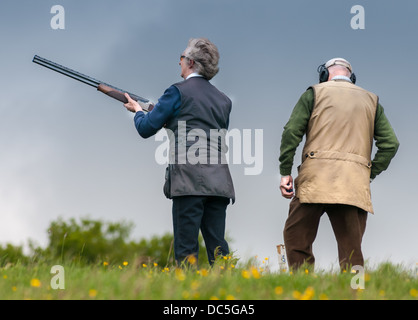 Lady shooting a shotgun at a simulated game and grouse clay shooting day, helped by a loader Stock Photo