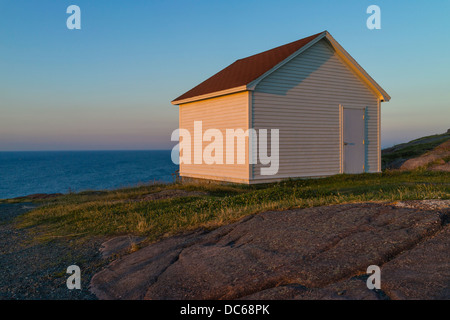 A simple white wooden structure without windows sits alone along the coast at the Cape Spear Lighthouse in Newfoundland.