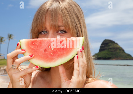 A woman holds up a slice of watermelon in front of her face. Stock Photo