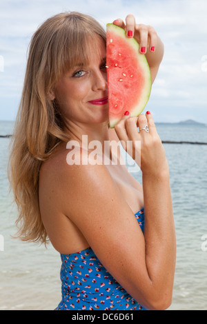 A woman holds up a slice of watermelon in front of her face. Stock Photo