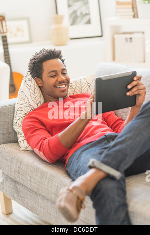 Man lying on sofa and using tablet PC Stock Photo