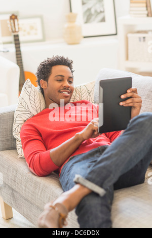 Man lying on sofa and using tablet PC Stock Photo