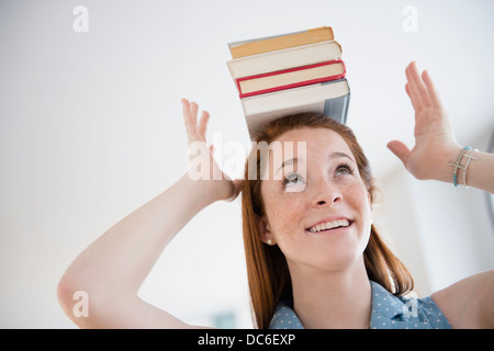 Teenage girl (14-15) holding stack of books on head Stock Photo