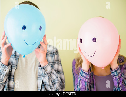 Studio shot of couple holding balloons with smiley faces in front of their heads Stock Photo