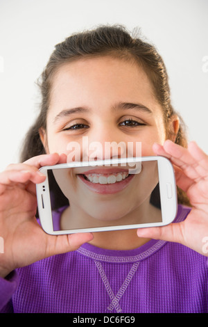 Studio shot of girl (8-9) holding smartphone with picture of her mouth Stock Photo