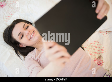 Portrait of young woman lying down on bed and holding digital tablet Stock Photo