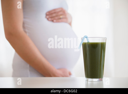 Mid section of pregnant woman, green smoothie in front Stock Photo