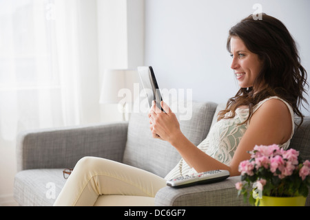 Young woman on sofa reading on digital tablet Stock Photo