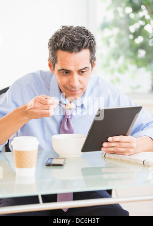 View of mature man eating cereal and using digital tablet Stock Photo