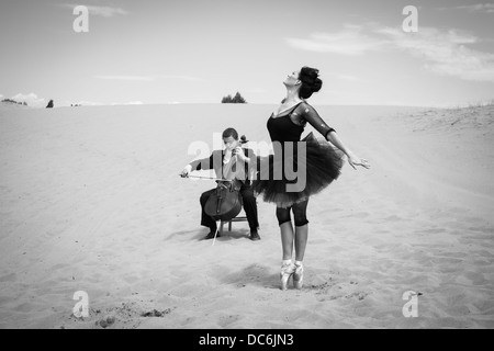 A solo cellist plays for an elegant ballerina dancing in the barren desert. Stock Photo