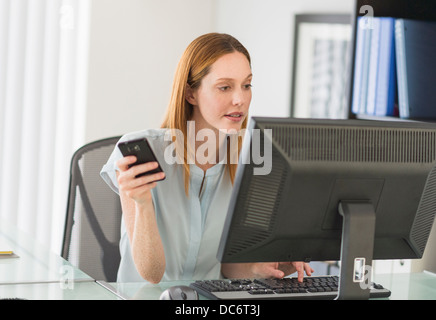 Business woman using computer and phone in office Stock Photo