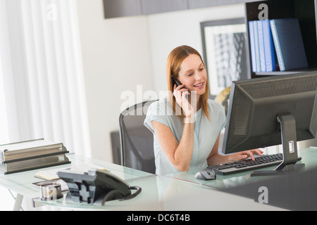 Business woman using computer and phone in office Stock Photo