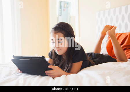 Girl (8-9) laying on bed and using digital tablet Stock Photo