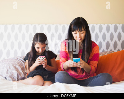 Mother with daughter (8-9) sitting and using cell phones Stock Photo